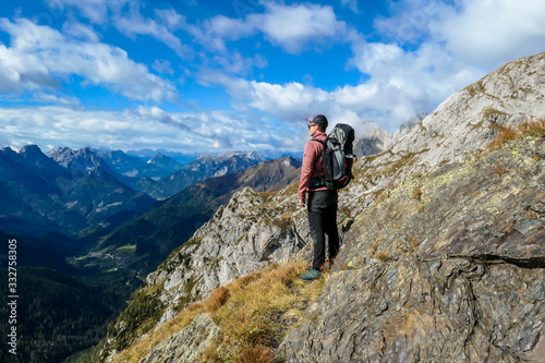 Man reaching the top of Monte Coglians, Hohe Warte on Austrian-Italian Alpine border. Very steep and narrow pathway that he walks on. He is enjoying the landscape. Goal visualization. Stunning view
