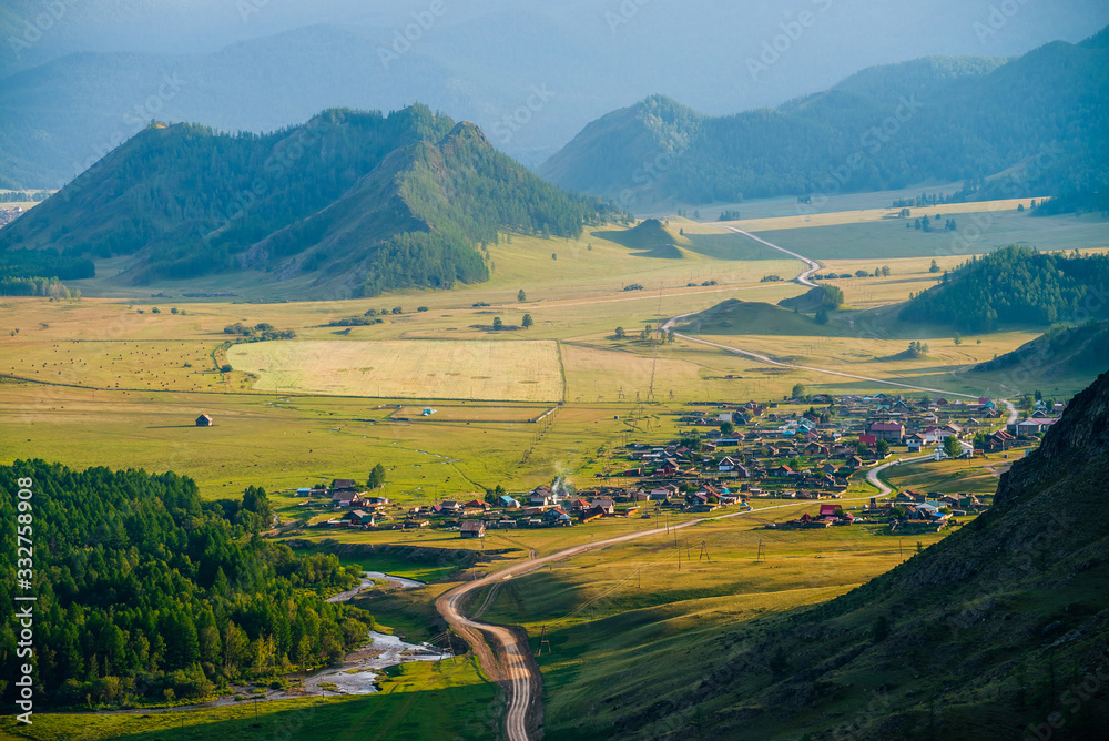 Wonderful view to village among great forest hills and mountains in evening light. Many small houses in sunlight. Beautiful green alpine countryside. Amazing mountain village. Country land at sunset.