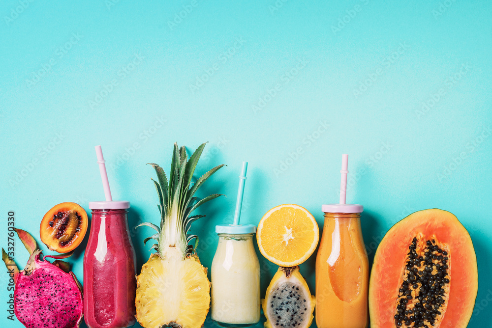 Colorful smoothie drink in glass bottle with straw and fruit ingredients -  papaya, orange, pineapple, dragon fruit, pitahaya, tamarillo fruit over  blue background. Top view, flat lay, copy space Stock Photo |