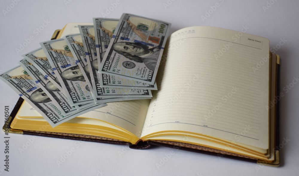 a diary with gold pen, a bunch of banknotes, US dollars lying on it on a white background a diary with gold pen, a bunch of banknotes, US dollars lying on it on a white background