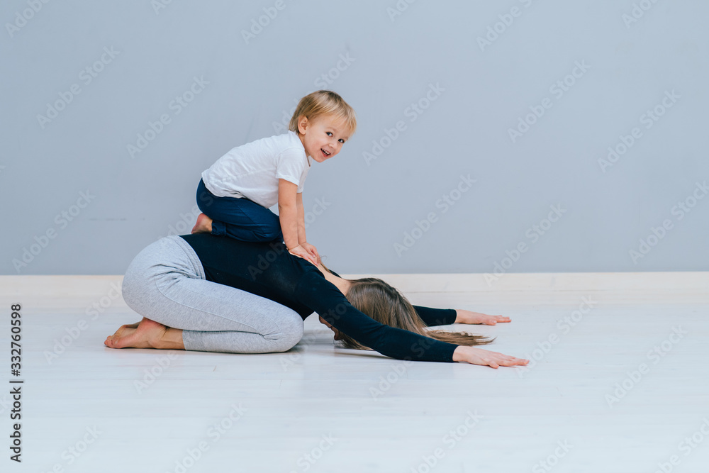 Fototapeta premium Beautiful mother and charming little daughter are smiling while practicing yoga together at home, making child's pose exercise, copy space