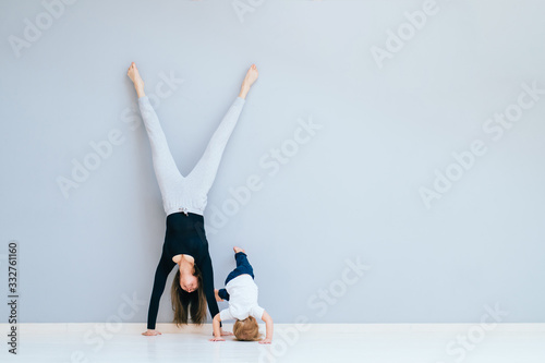 Sportive brunette mother with baby son doing press exercise on grey yoga mat over gray wall background. Athletic and healthy motherhood. Fitness, happy maternity and healthy lifestyle concept. photo