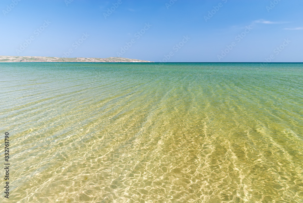 Clear turquoise sea with solar reflections and far coast in the background