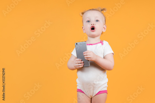 little girl holds the phone and makes a funny face. Isolated on yellow-orange