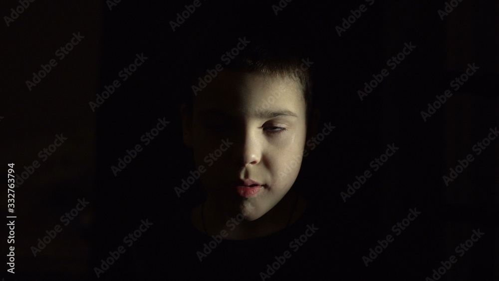 The boy's face is illuminated. Closed eyes. Dark room. Horror. Scary tale. Close-up. The boy's face is illuminated. Closed eyes. Dark room. Horror. Scary tale. Close-up.