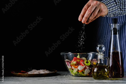 A cook pours salt into a salad . Healthy food and vegetarianism.On a black background in a glass bowl.