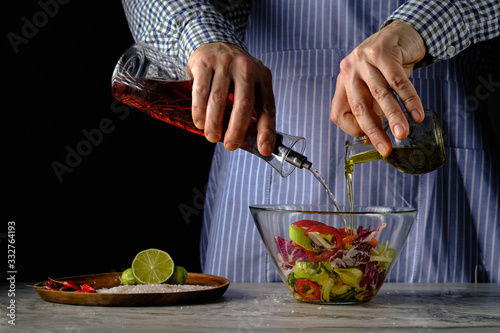 A cook pours olive oil into a salad and balsamic vinegar. Healthy food and vegetarianism.On a black background in a glass bowl.