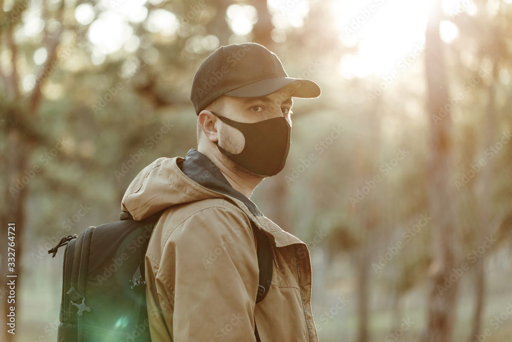 confident optimistic man in medical mask walks through forest with backpack