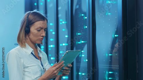 Smart woman IT administrator visually inspecting operative server cabinets in digital room. Female tech support talking on headset coworking in data center security.
