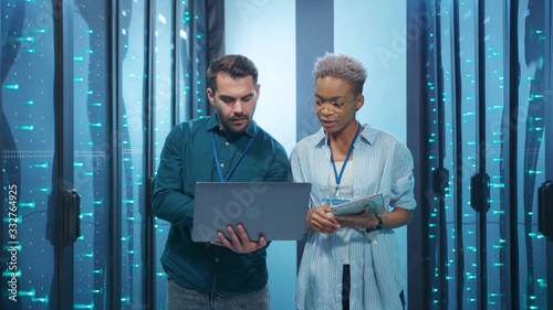 Professional diverse team of data center specialists coworking in server room. Female and male engineers inspecting internet database servers at computer security. Teamwork.
