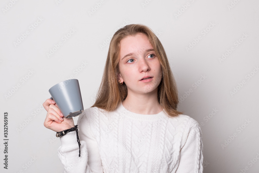 Charming girl with a mug of tea. Cute teenager girl with blond hair holds a mug. Girl drinks from a mug. Charming girl with a mug of tea. Cute teenager girl with blond hair holds a mug. Girl drinks from a mug.