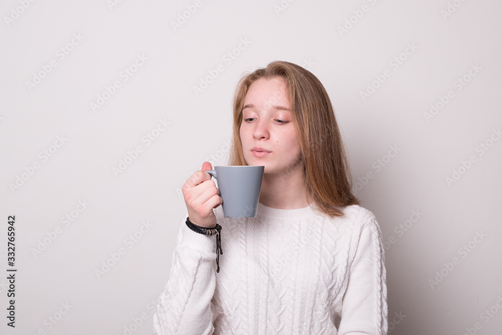 Charming girl with a mug of tea. Cute teenager girl with blond hair holds a mug. Girl drinks from a mug. Charming girl with a mug of tea. Cute teenager girl with blond hair holds a mug. Girl drinks from a mug.