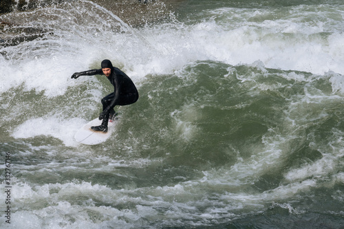 Man in black wetsuit surfing On Eisbach River Germany, Munich, Englischer Garden during winter