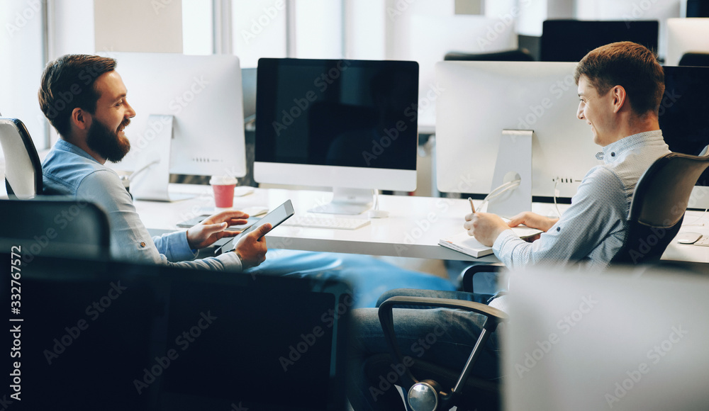 Side view photo of two caucasian men having a business discussion in their office while using a tablet