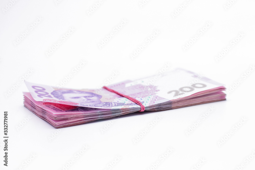 A lot of new banknotes in denominations of 200 Ukrainian hryvnias bandaged with an elastic band isolated on a white background with shadow. European money exchange. Ukraine currency. Selective focus A lot of new banknotes in denominations of 200 Ukrainian hryvnias bandaged with an elastic band isolated on a white background with shadow. European money exchange. Ukraine currency. Selective focus