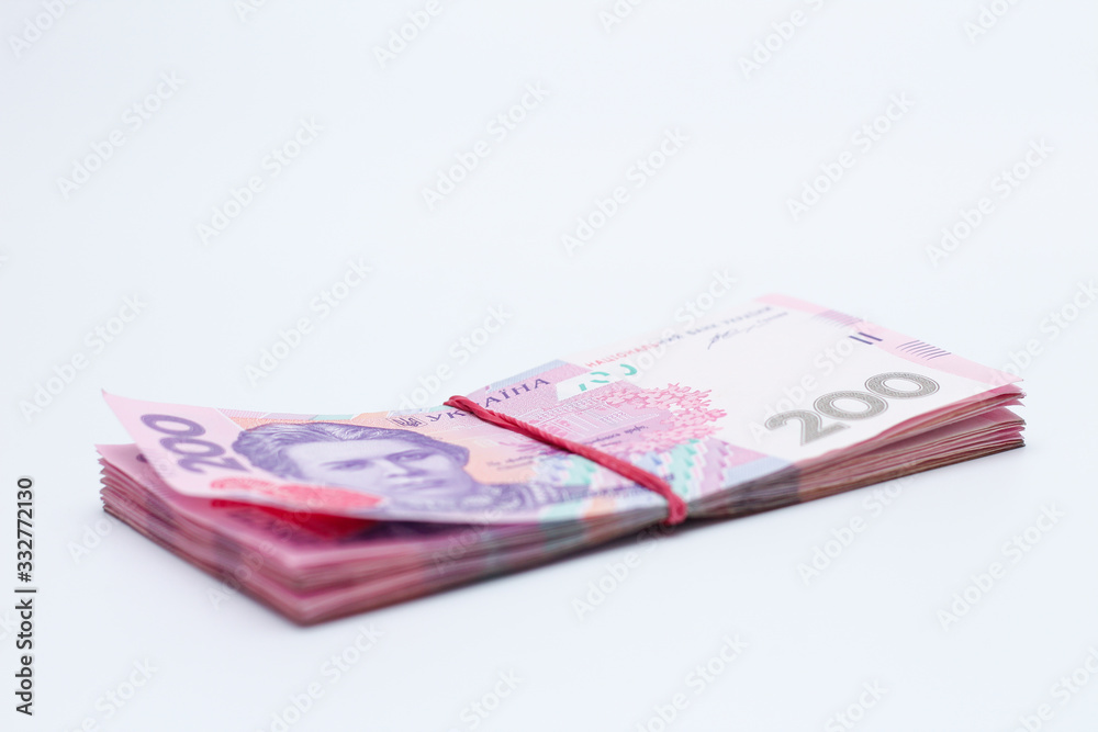 A lot of new banknotes in denominations of 200 Ukrainian hryvnias bandaged with an elastic band isolated on a white background with shadow. European money exchange. Ukraine currency. Selective focus A lot of new banknotes in denominations of 200 Ukrainian hryvnias bandaged with an elastic band isolated on a white background with shadow. European money exchange. Ukraine currency. Selective focus
