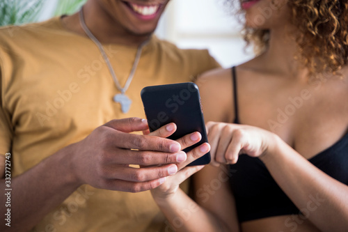 Detail of online dating application for young people. Afro culture lifestyle with technology at home. Millennial african american couple looking the smart phone screen and preparing holidays.