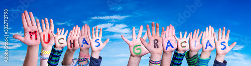 Children Hands Building Colorful Spanish Word Muchas Gracias Means Thank You. Blue Sky As Background
