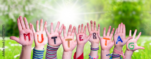 Children Hands Building Colorful German Word Muttertag Means Mother Day. Sunny Green Grass Meadow As Background photo