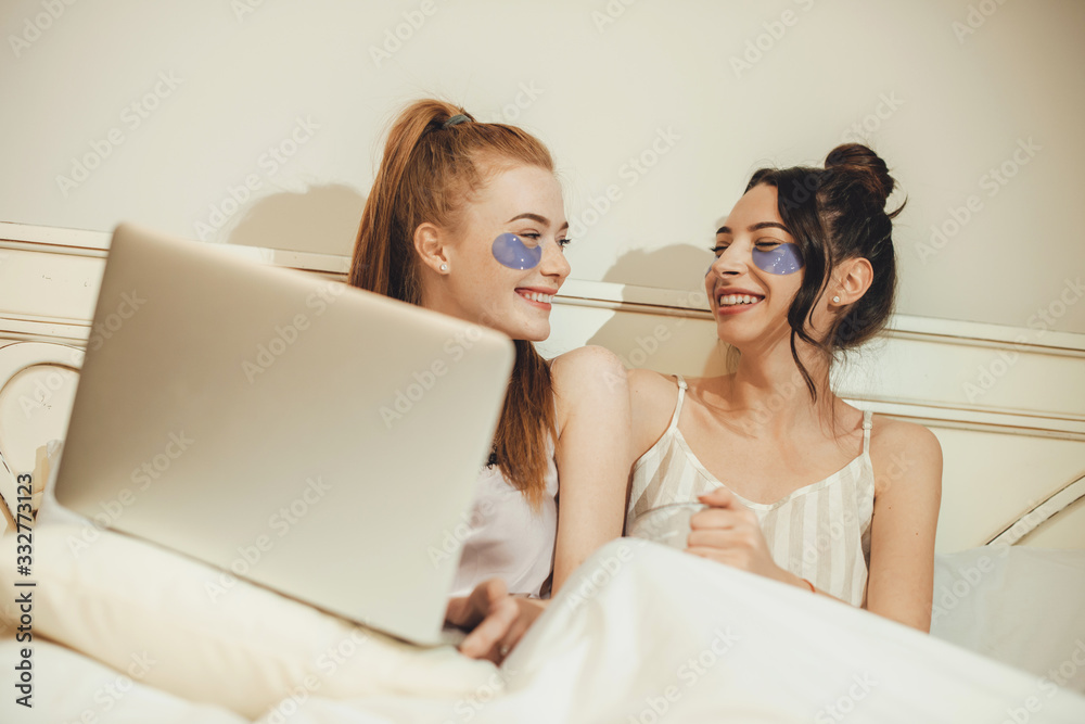 Two caucasian sisters wearing some anti aging masks while lying in the bed with a computer Two caucasian sisters wearing some anti aging masks while lying in the bed with a computer