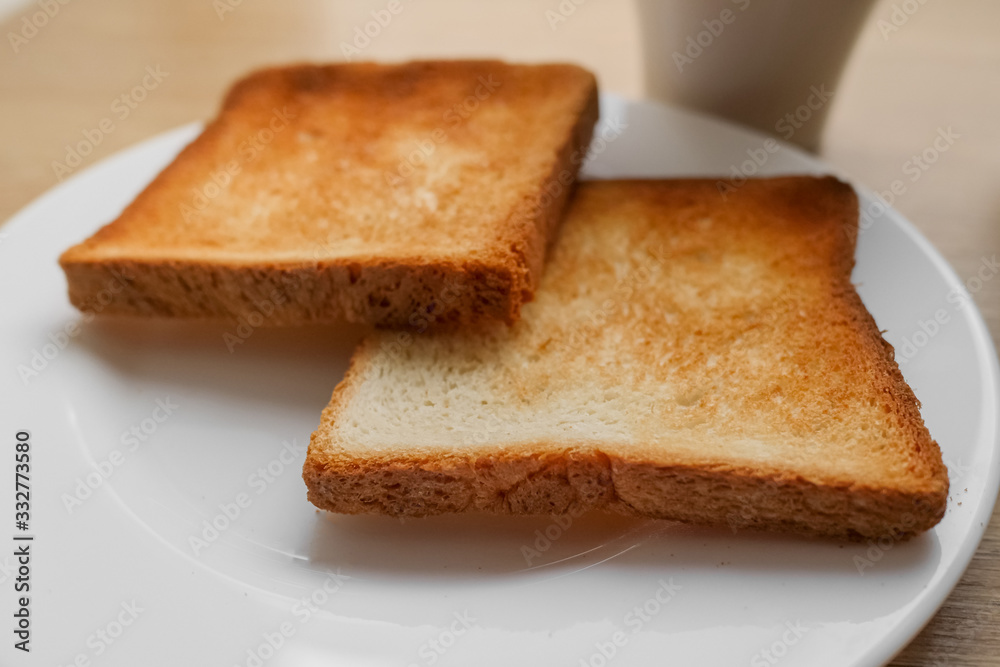 two pieces of toasted sliced bread on a white plate and coffee on wooden table, ready to do sandwich for breakfast. selective focus.