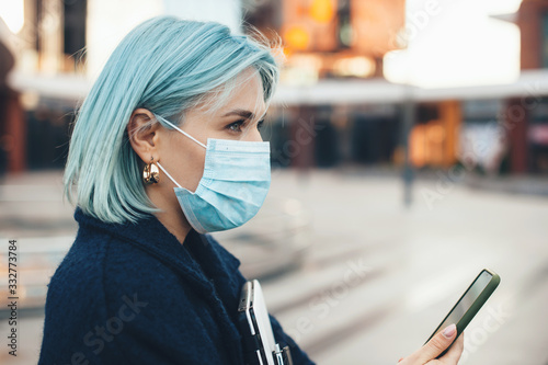Gorgeous caucasian entrepreneur with blue hair posing with modern gadgets while wearing an anti flu mask