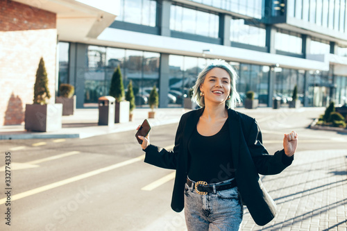 Happy caucasian woman with blue hair cheering outside while holding a mobile