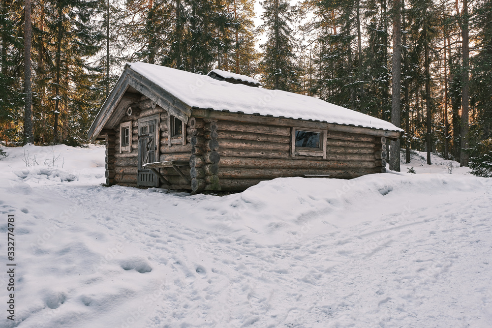 Small wooden cabin with snow on the roof and ground and forest in the background