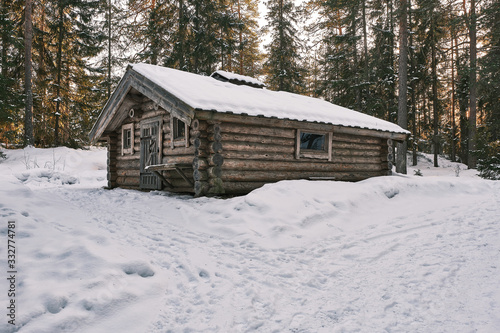 Small wooden cabin with snow on the roof and ground and forest in the background © Kilman Foto