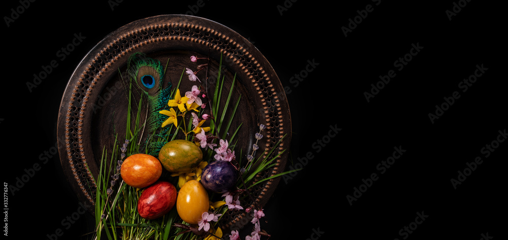 Colored easter Eggs in a plate with black background and copy space. With grass