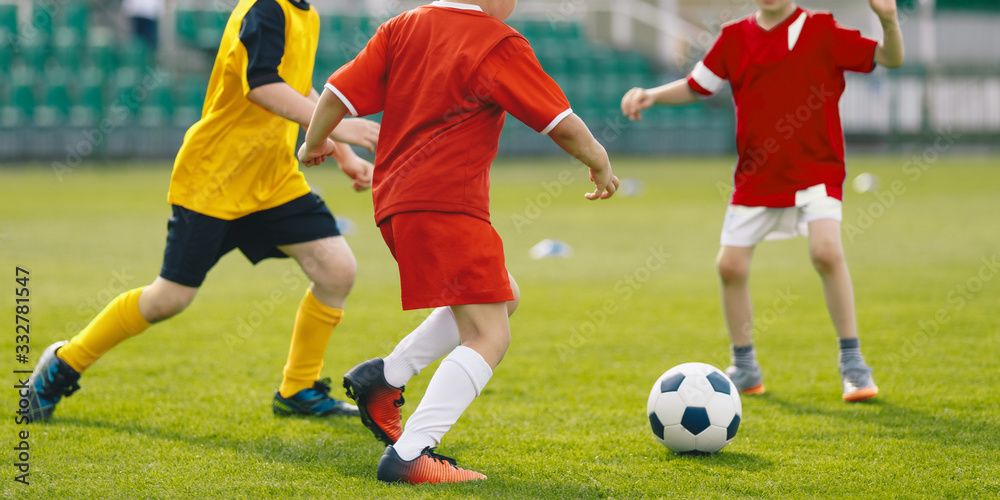 Children play soccer game on grass venue. Kids kicking soccer ball. Boys in red and yellow soccer jersey and soccer cleats Children play soccer game on grass venue. Kids kicking soccer ball. Boys in red and yellow soccer jersey and soccer cleats