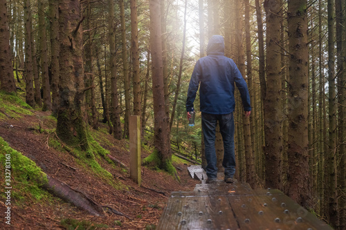 Man on a walk in a forest on a rainy day, Wet wooden walk path, bottle of fresh water in his hands, sun flare, Concept outdoor activity,