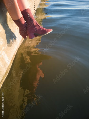 Legs of a woman with red boots sitting on a dock at a lake