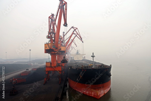 Cargo terminal for discharging coal cargos by shore cranes during foggy weather. Port Bayuquan,China. January, 2020.