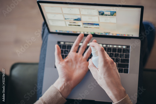 man sprinkles an antiseptic on his hand near a silver laptop