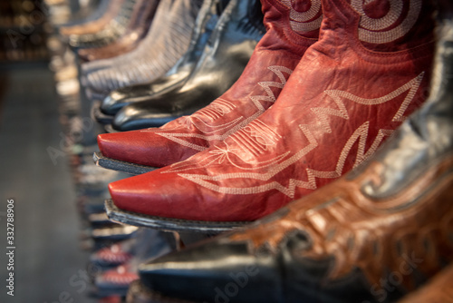 A row of new shiny men's cowboy boots lined up on a shelf.The boots have a decorative stitching.