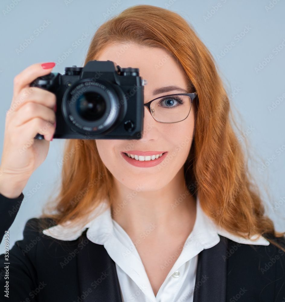 Young redhead woman holding a camera. She is wearing glasses and a suit. Young redhead woman holding a camera. She is wearing glasses and a suit.