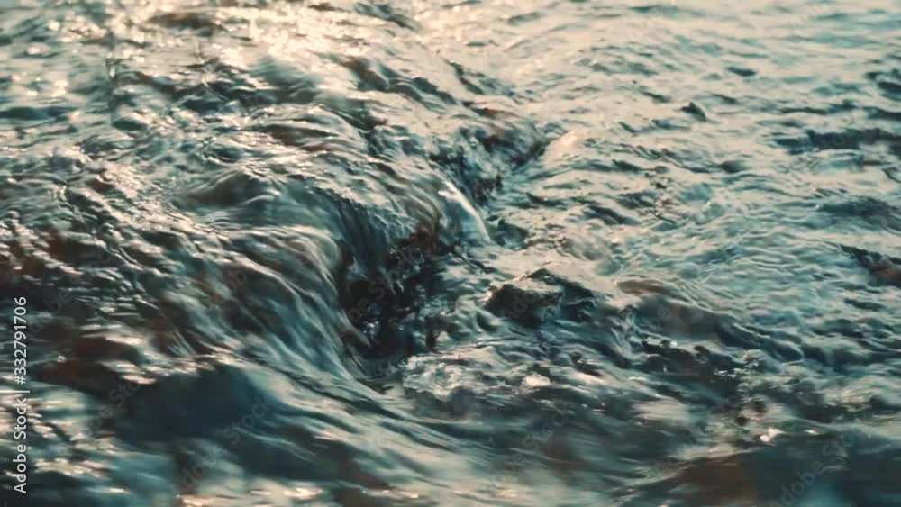 Fast moving water, passing by stones. Close-up. Creek in turquoise color Fast moving water, passing by stones. Close-up. Creek in turquoise color