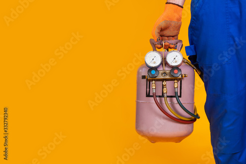 A male air conditioner repairman is holding a freon cylinder and a pressure measurement sensor in his hand for air conditioning refilling. photo