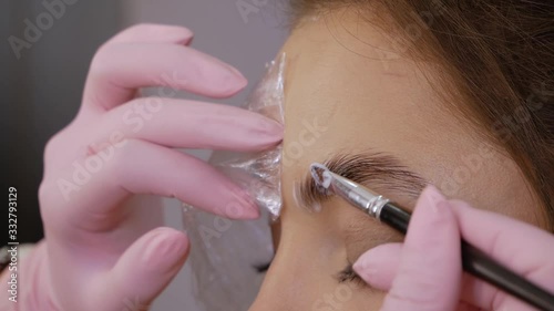 Part of the eyebrow lamination procedure. Female beautician hand applies paint with a brush on the eyebrows of a beautiful patient