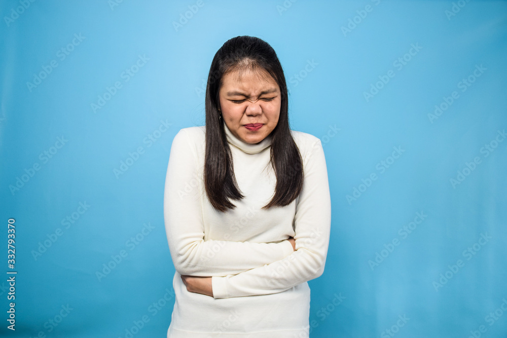 Portrait of Young beautiful asian women using white T-shirt with blue isolated background, stomachache Portrait of Young beautiful asian women using white T-shirt with blue isolated background, stomachache