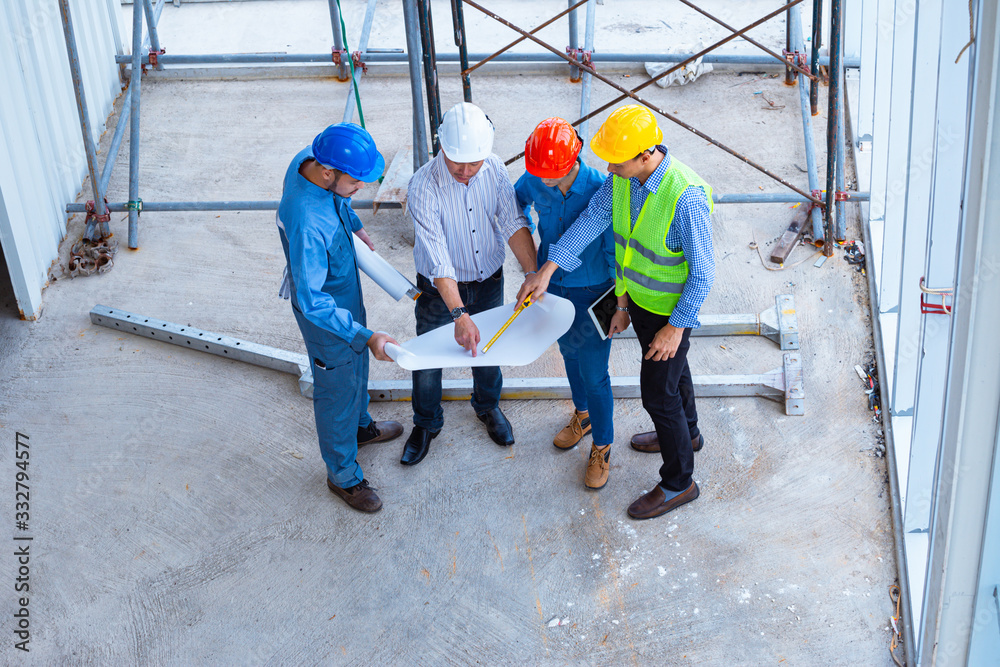 Top view of architectural engineer working on his blueprints with documents on construction site. meeting, discussing,designing, planing, serious civil engineer working Top view of architectural engineer working on his blueprints with documents on construction site. meeting, discussing,designing, planing, serious civil engineer working