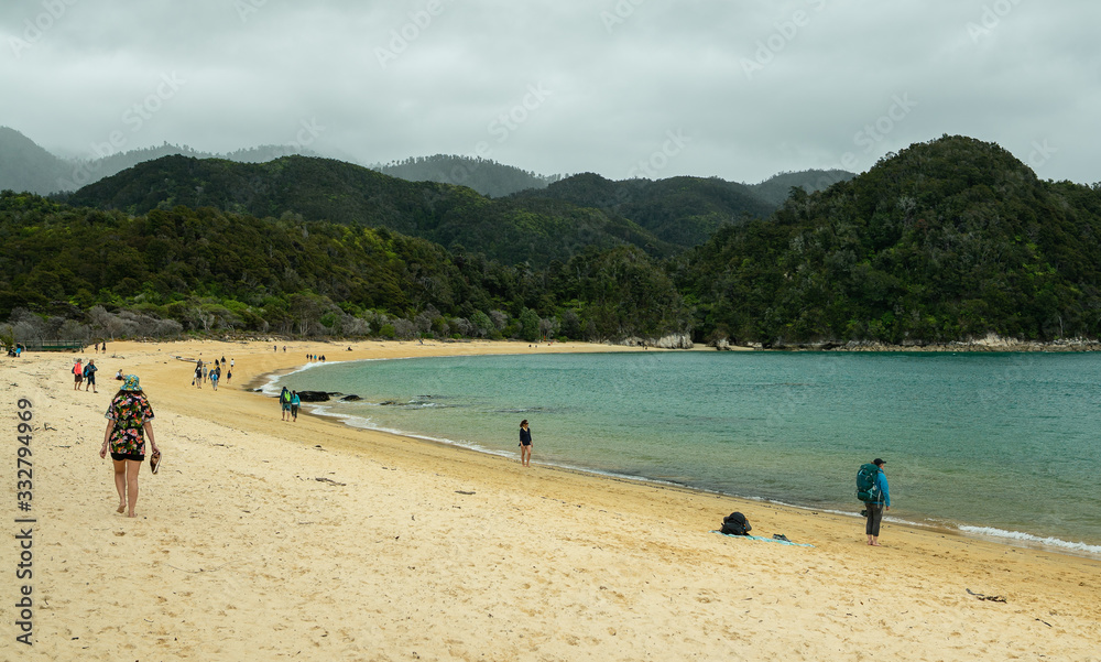 People walking on beach next to rainforest at Anchorage Bay New Zealand People walking on beach next to rainforest at Anchorage Bay New Zealand
