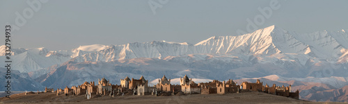 first morning sunlight falling on the cemetery of Terek, south of Baetov, near the Mels-Ashu pass with the amazing landscape of the  Tian Shan mountains covered in snow around photo