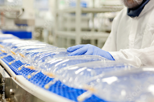 Medical personnel and lab workers wearing gloves work at a conveyor belt producing IV bags for medical care. 