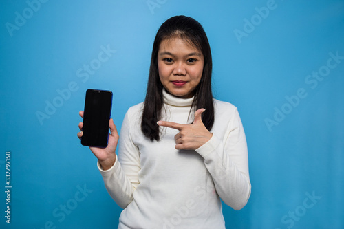 Portrait of Young beautiful asian women with blue isolated background,showing blank screen mobile phone, good apps, recomended apps photo