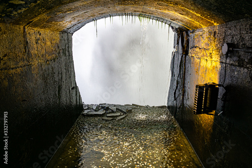 Fotografie A tunnel behind a falls and coins in the waters