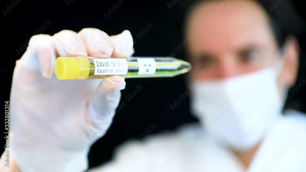 Selective focus shot of vial filled with liquid, label Covid-19 test held by nurse. Figure pulls sample back rack focus to reveal male doctor's face. Selective focus shot of vial filled with liquid, label Covid-19 test held by nurse. Figure pulls sample back rack focus to reveal male doctor's face.