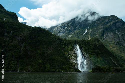 Rolling clouds over mountains and waterfall going into lake at Milford Sound New Zealand