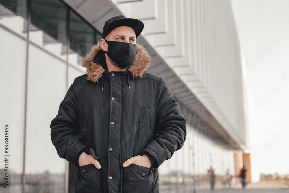 Naklejka premium Men wears a black protective medical face mask being in the city during a coronavirus pandemic. Protection from viruses in the city.